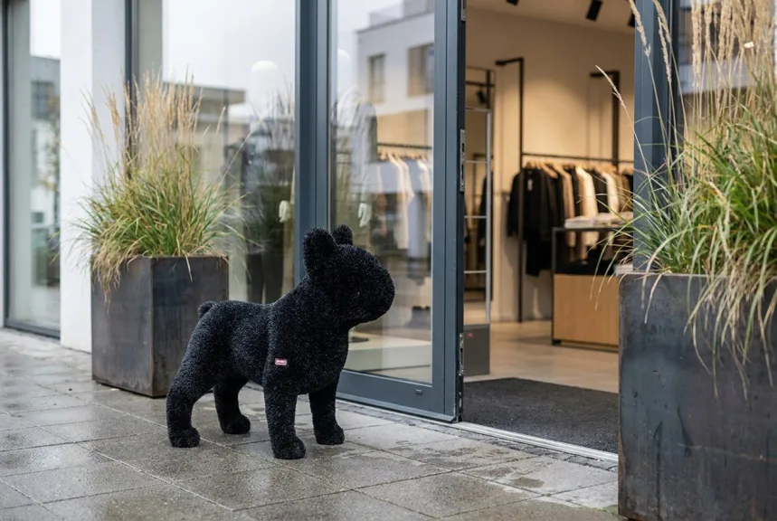 A black turf covered dog sculpture beside the glass entrance of a shop